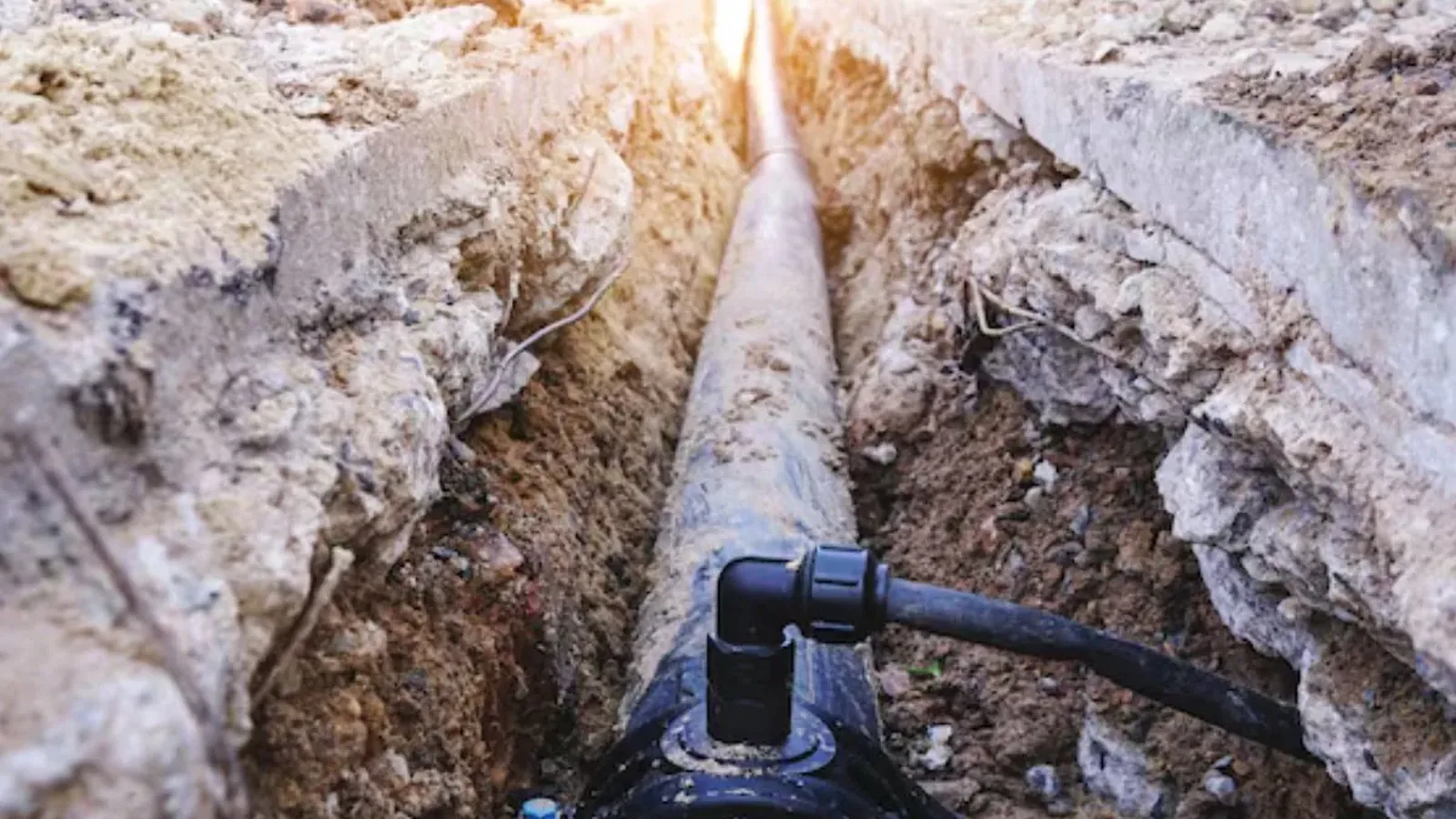 Exposed water service line in an excavated trench with a pipe fitting